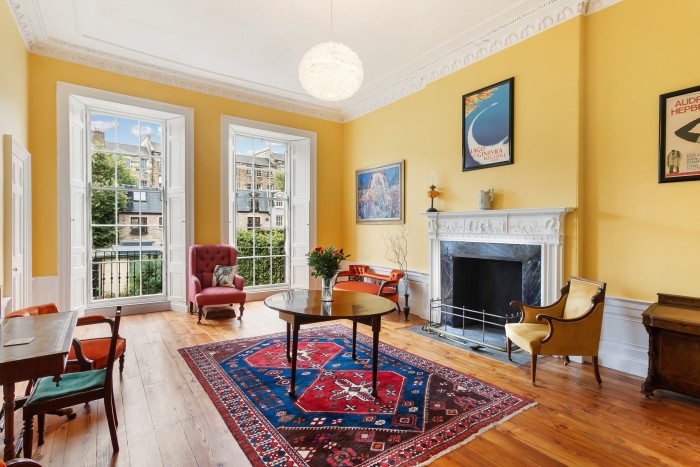 A bright living room with yellow walls, tall windows and a fireplace