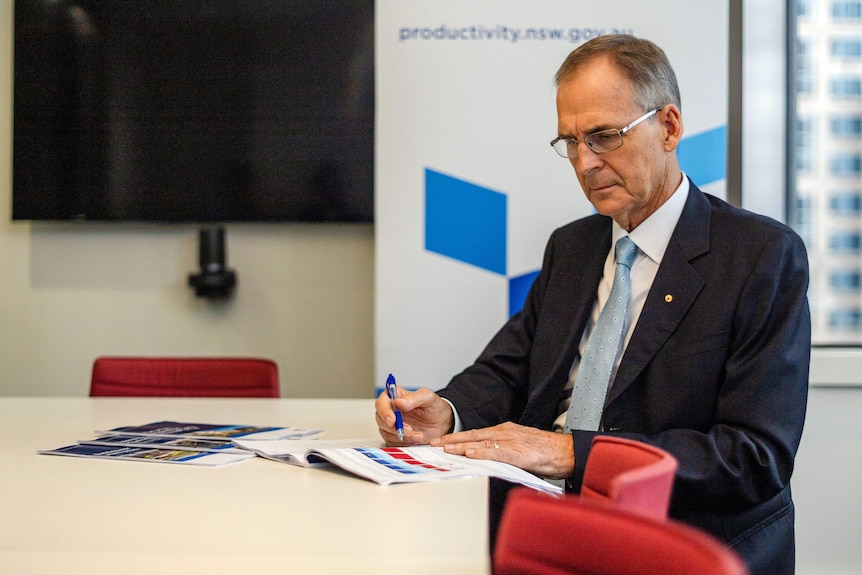 Peter Achterstraat the NSW Productivity Commissioner sits at a desk overlooking a report on housing