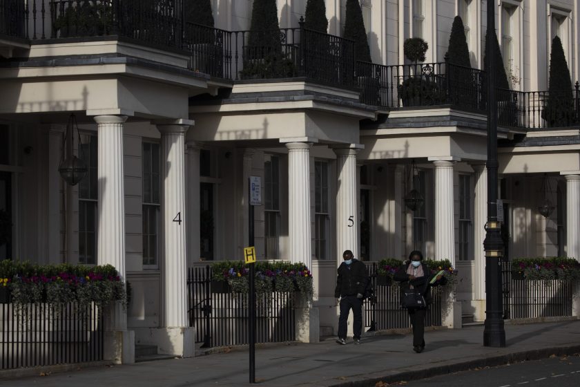Pedestrians wearing protective face masks walk past columns of residential houses in the Belgravia district of London.