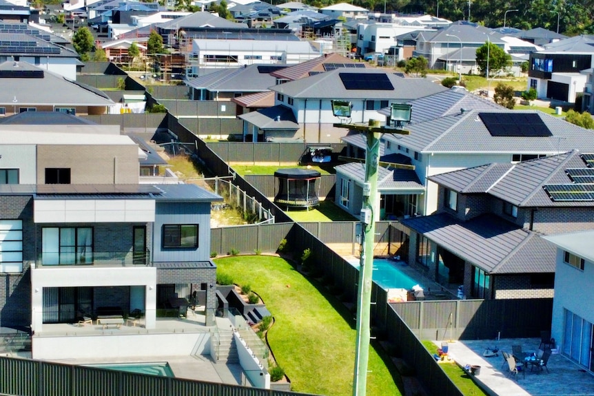 An aerial view of backyards of houses in a new housing estate with pools and green lawns.