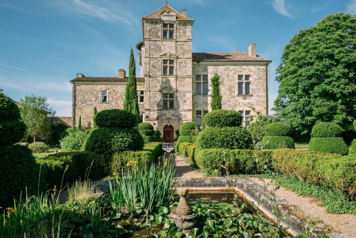 A stone château with a towering centre and landscaped gardens under a blue sky