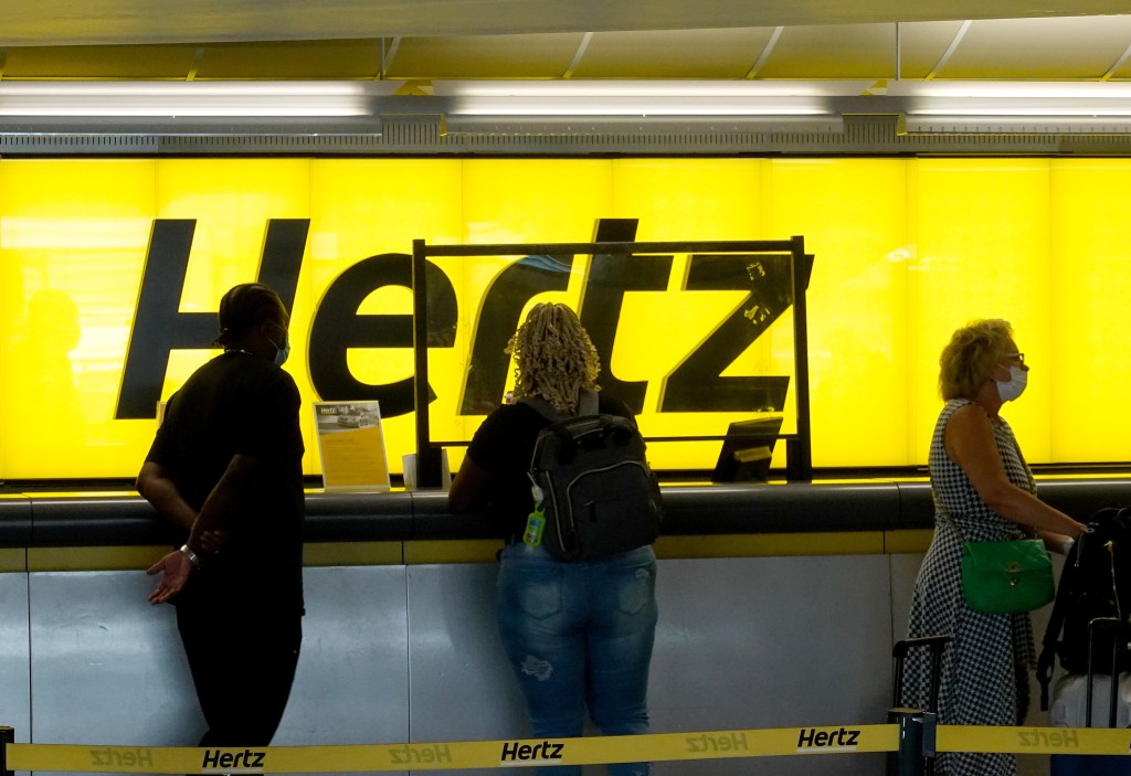 People wait in line at a Hertz rental car counter.